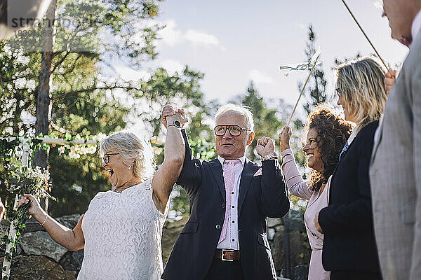 Glückliches Ehepaar hält sich an den Händen und tanzt mit der Familie bei der Hochzeitszeremonie