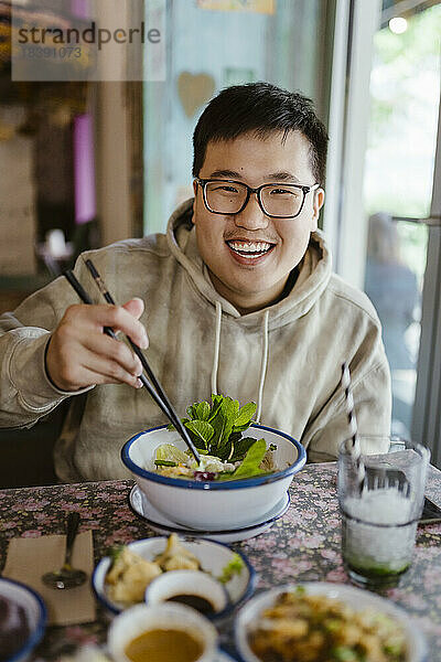 Porträt eines lächelnden jungen Mannes mit Essen und Stäbchen in einem Restaurant