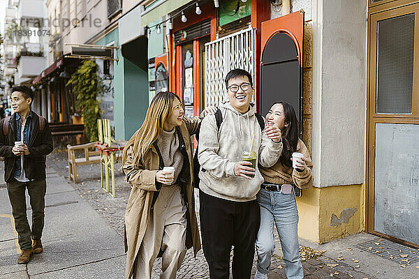 Fröhliche männliche und weibliche Freunde unterhalten sich beim Gehen auf dem Bürgersteig