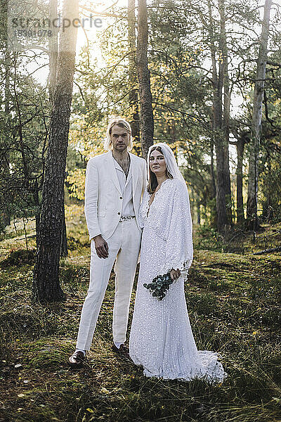 Porträt von gut gekleideten Braut und Bräutigam stehen durch Bäume im Wald bei der Hochzeit