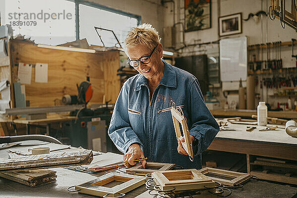 Lächelnder Senior-Tischler bei der Prüfung von Rahmen in der Werkstatt