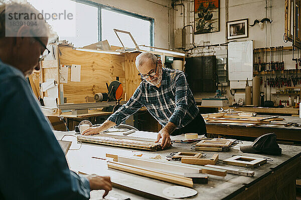 Älterer männlicher Zimmermann prüft Holz auf einer Werkbank in einer Reparaturwerkstatt