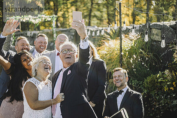 Glücklicher älterer Mann  der ein Selfie mit der Braut und der Familie auf einem Smartphone während der Hochzeitszeremonie macht