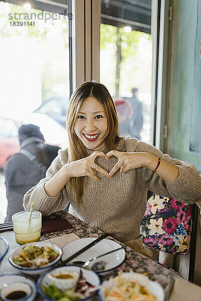 Porträt einer glücklichen Frau  die eine herzförmige Geste macht  während sie im Restaurant sitzt