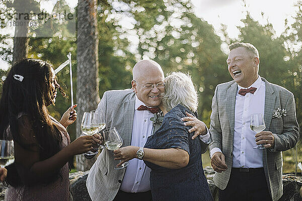 Glatzköpfiger älterer Bräutigam umarmt seine Freundin beim Weintrinken auf der Hochzeitsfeier