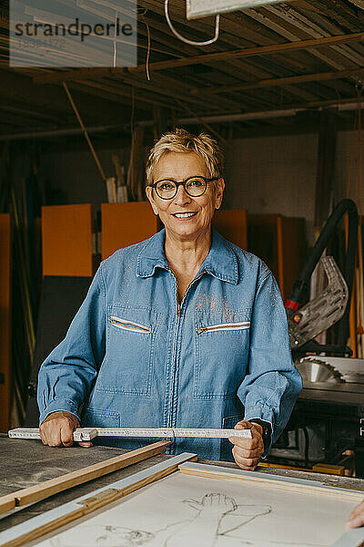 Porträt einer lächelnden älteren Handwerkerin mit Maßband in der Werkstatt