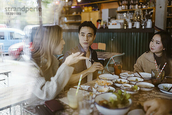 Männliche und weibliche Freunde  die sich in einem Restaurant unterhalten  gesehen durch ein Glasfenster