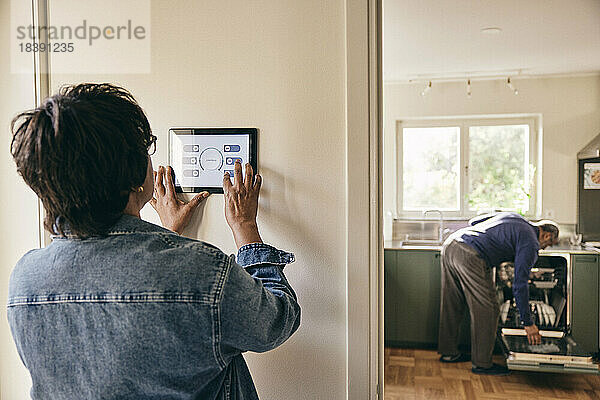 Ältere Frau in Jeansjacke  die die Hausautomatisierung an der Wand benutzt