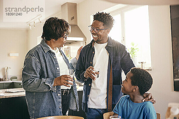 Ältere Frau mit einem Glas Wasser im Gespräch mit Sohn und Enkel zu Hause