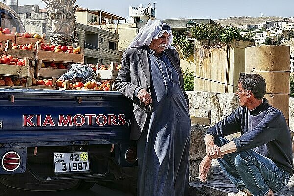 älterer Mann mit Turban und traditionelle Kleidung  Tomatenhändler unterhält sich mich hockendem Mann.  Jordanien. Tomaten  Verkauf
