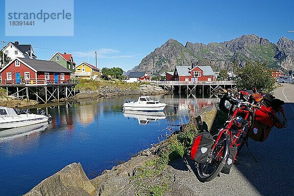Verschieden farbige Hozhäuser spiegeln sich in glasklarem Meereswasser  bepacktes Reiserad  Fahrradtourismus  kleine Freizeitboote und Rorbuer  Henningsvaer  Lofoten  Nordland  Norwegen  Europa