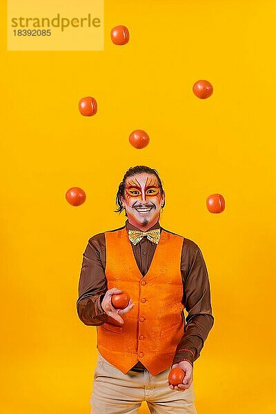 Jongleur in Weste und mit bemaltem Gesicht jongliert Bälle auf einem gelben Hintergrund