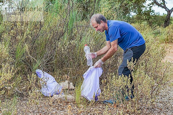 Mann mit Müllsäcken und Handschuhen beim Säubern des Busches von verunreinigenden Abfällen