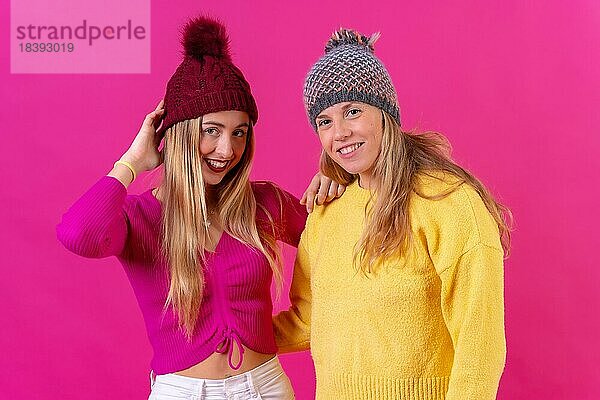 Zwei blonde kaukasische Frauen mit Wollmützen auf einem rosa Hintergrund  Porträtblick