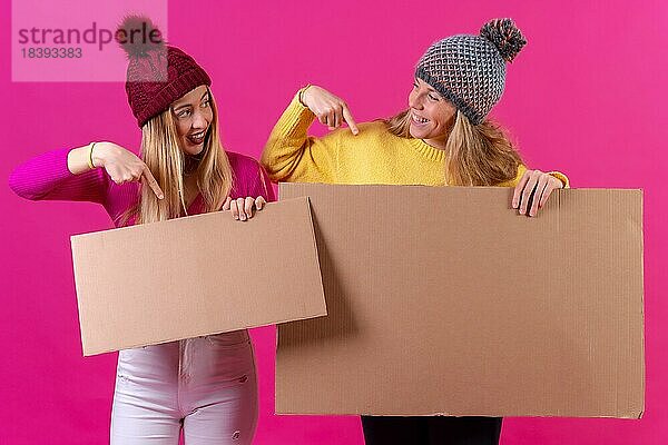 Zwei junge blonde kaukasische Frauen halten ein Schild vor einem rosa Hintergrund  Studioaufnahme  die auf