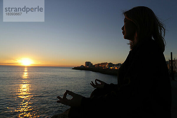 Frau bei Yoga-Meditation am Meer bei Sonnenuntergang als Konzept für Ruhe und Entspannung  Cadiz  Andalusien  Spanien  Europa