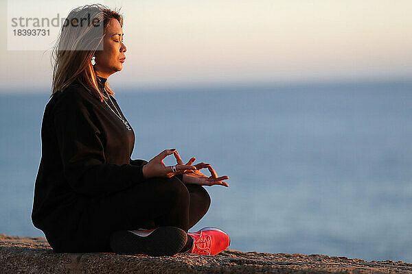 Frau bei einer Yoga-Meditation am Meer vor Sonnenuntergang als Konzept für Ruhe und Entspannung  Spanien  Europa