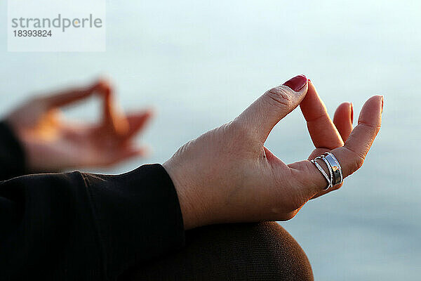 Frau praktiziert Yoga-Meditation am Meer bei Sonnenuntergang als Konzept für Stille und Entspannung  Nahaufnahme auf Hand  gyan mudra  Spanien  Europa