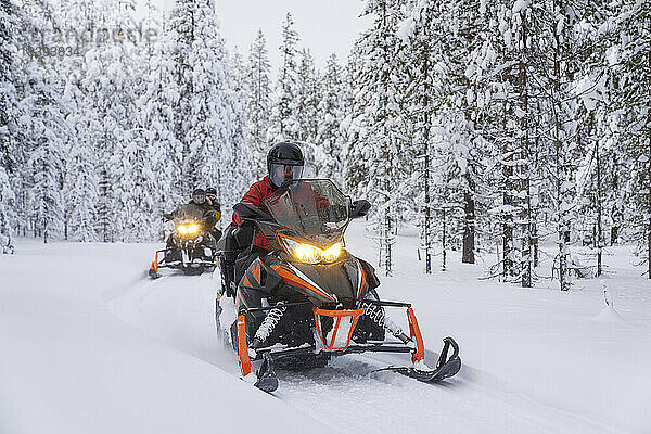 Drei Personen fahren Motorschlitten  eingerahmt von gefrorenen Bäumen im verschneiten Wald  Lappland  Schweden  Skandinavien  Europa
