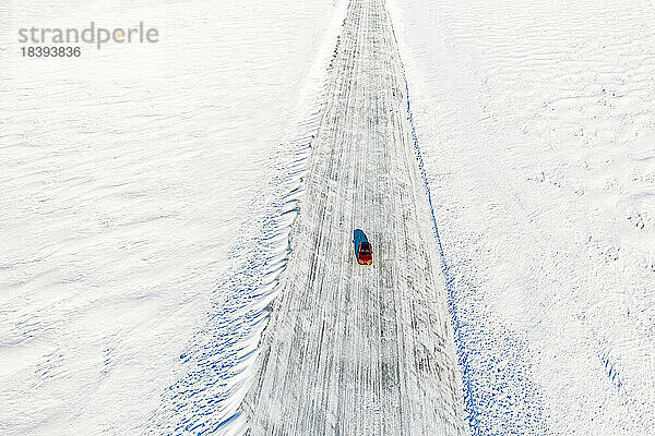 Kalte Wintersonne über einem einsamen Auto  das auf einer Eisstraße auf dem zugefrorenen Meer fährt  Luftaufnahme  Lulea  Landkreis Norrbotten  Lappland  Schweden  Skandinavien  Europa