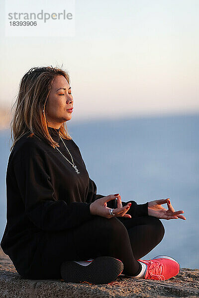 Frau bei einer Yoga-Meditation am Meer vor Sonnenuntergang als Konzept für Ruhe  Harmonie und Entspannung  Spanien  Europa