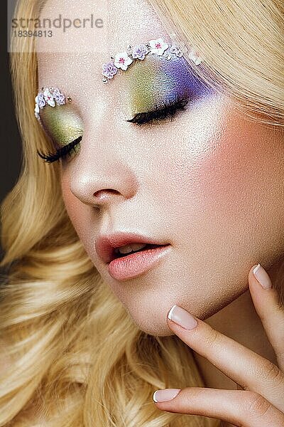 Schöne junge blonde Frau mit kreativen Make up Farbe  Locken und Blumen auf Augenbrauen. Schönheit Gesicht. Kunst Make up. Fotos im Studio geschossen