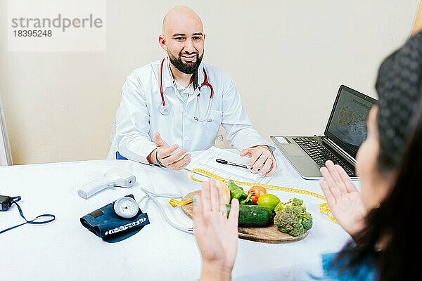 Ernährungsberater im Gespräch mit einer Patientin im Büro. Rückenansicht einer Patientin im Gespräch mit dem Ernährungsberater. Lächelnde Ernährungsberaterin  die einer Patientin etwas erklärt