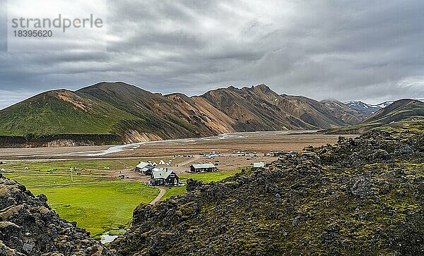 Campingplatz und Hütte Landmannalaugar  Lavafeld Laugahraun  hinten bunte Rhyolith Berge  Vulkanlandschaft  bunte Erosionslandschaft mit Bergen  Landmannalaugar  Fjallabak Naturreservat  isländisches Hochland  Suðurland  Island  Europa