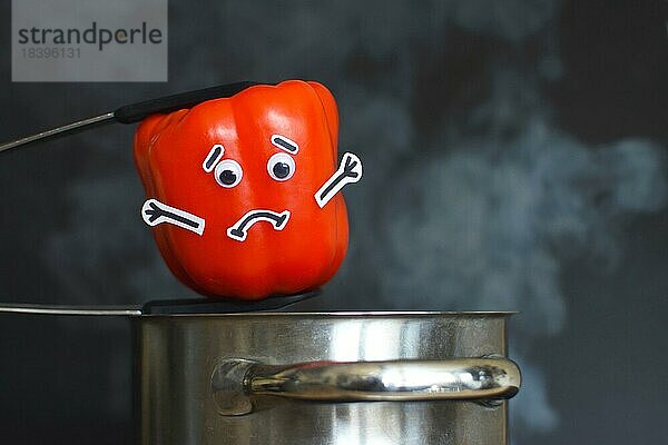 Rote Paprikaschote mit traurigem Gesicht und Glotzaugen  die in einen dampfenden Kochtopf auf dunklem schwarzem Hintergrund gelegt wird  Konzept für Gemüse  das beim Kochen Vitamine verliert
