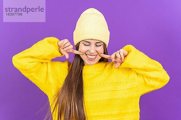 Close up Porträt einer jungen  fröhlichen Frau vorlila Studio Hintergrund in gelben Wollpullover lächelnd