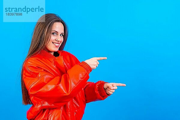 Attraktive Frau lächelnd zeigt mit den Fingern auf Kopie Raum auf blauem Hintergrund  rote Windjacke