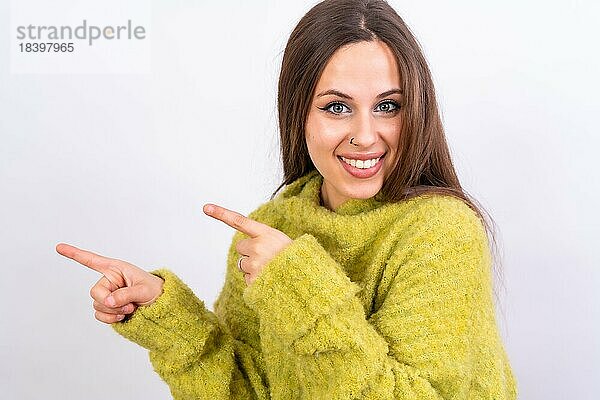 Attraktive Frau  die lächelnd mit den Fingern auf den Kopierraum auf weißem Hintergrund zeigt  grüner Wollpullover