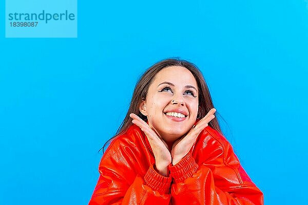 Close up Porträt einer jungen Frau  fröhlich oder lachend vorblauem Studio Hintergrund in roter Windjacke