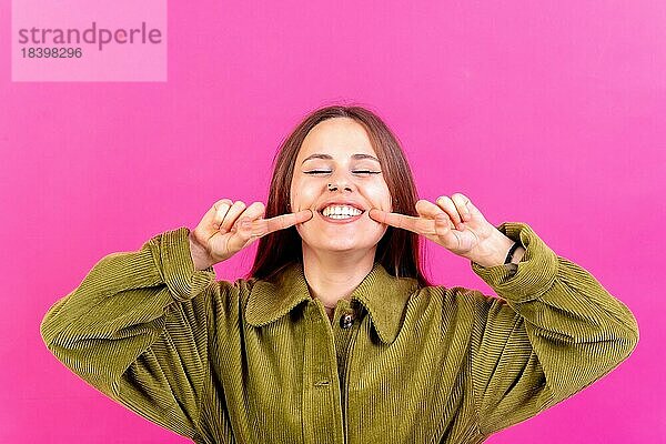 Close up Porträt der jungen Frau  fröhlich oder lachend vorrosa Studio Hintergrund in grüner Windjacke