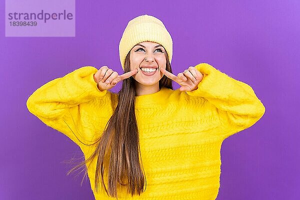 Close up Porträt einer jungen  fröhlichen Frau vorlila Studio Hintergrund in gelben Wollpullover lächelnd