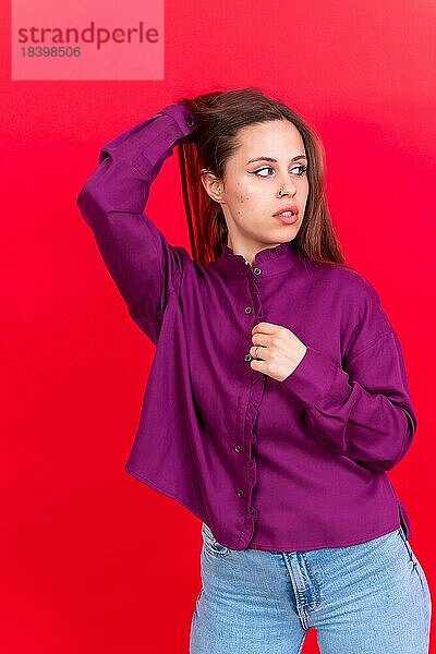 Close up Porträt der jungen kaukasischen Frau in lila Shirt vor rotem Hintergrund Studio