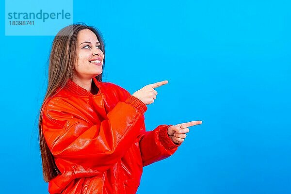 Attraktive Frau lächelnd Zeigefinger auf Kopie Raum auf blauem Hintergrund  rote Jacke sehr fröhlich