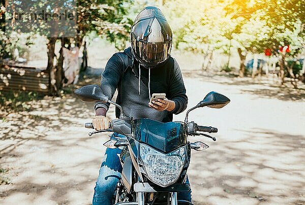 Mann auf Motorrad  der während der Fahrt eine SMS schreibt. Motorradfahrer auf Motorrad mit Handy im Freien. Konzept eines abgelenkten Motorradfahrers mit Mobiltelefon