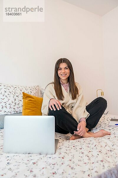 Porträt einer Frau  die mit einem Laptop auf dem Bett sitzend arbeitet  Telearbeit