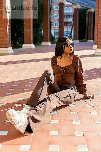 Eine schöne junge afrikanische Frau in einem Park  Lifestyle. Modisch posiert  auf dem Boden sitzend bei Sonnenuntergang