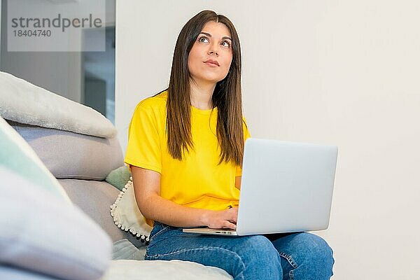 Frau mit einem Computer auf einem Sofa sitzend  Millennial  soziale Netzwerke  nachdenklich mit einem Online Verkauf
