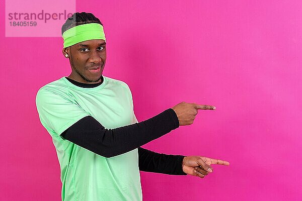 Schwarzer ethnischer Mann in grüner Kleidung auf rosafarbenem Hintergrund  der auf einen freien rechten Kopierraum zeigt