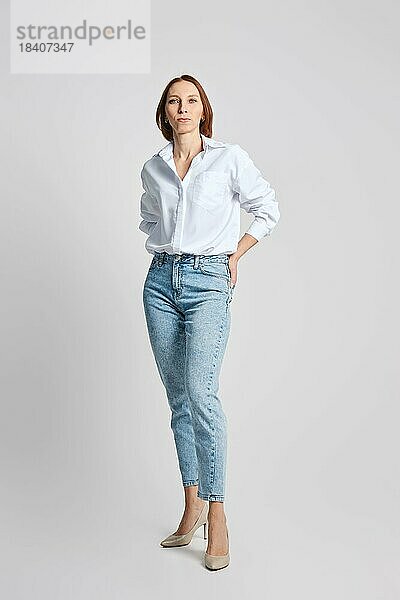 Attraktive Frau mittleren Alters in weißem Hemd steckt ihre Handflächen in die Gesäßtaschen ihrer Blue Jeans