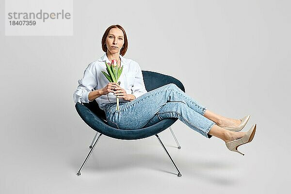 Atelierbildnis einer fröhlichen  mittelalten Frau im Sessel mit Tulpen in der Hand