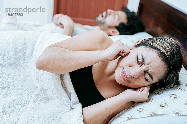 Ehefrau leidet unter dem Schnarchen ihres schlafenden Mannes. Schlafapnoe Konzept  Mann schnarcht im Schlafzimmer und Frau hält sich die Ohren zu