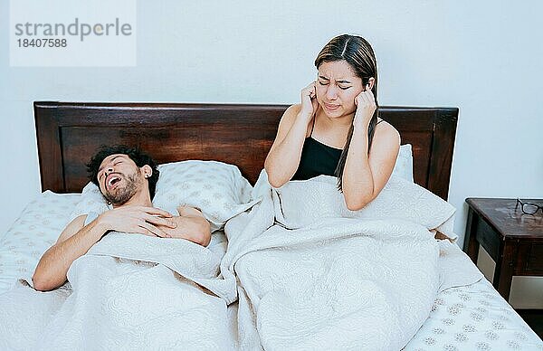 Ehemann schnarcht  während die Frau leidet und sich die Ohren zuhält. Schlafapnoe Konzept  Schnarchender Mann im Schlafzimmer und Frau hält sich die Ohren zu