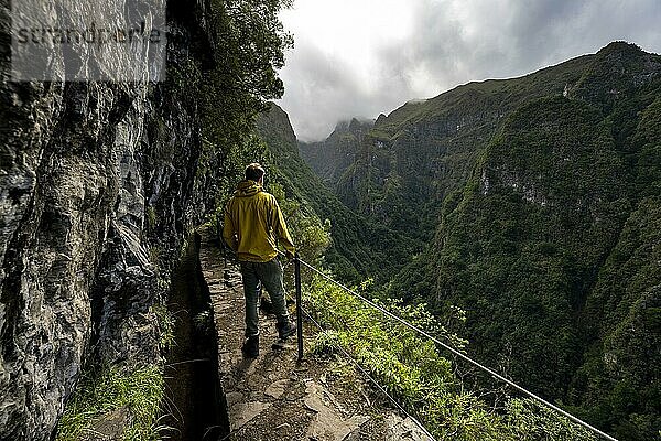Wanderer an einem schmalen Wanderweg entlang einer Levada  Ausblick auf bewaldete Berge  Levada do Caldeirão Verde  Parque Florestal das Queimadas  Madeira  Portugal  Europa