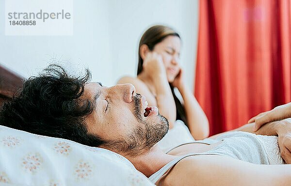 Schnarchender Mann im Schlafzimmer und Frau hält sich die Ohren zu. Ehemann schnarcht  während die Frau leidet und sich die Ohren zuhält. Schlafapnoe Konzept