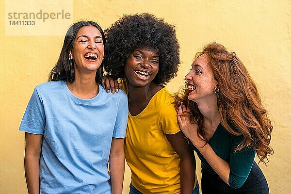 Porträt von schönen multiethnischen Freundinnen lächelnd auf einer gelben Wand Spaß haben
