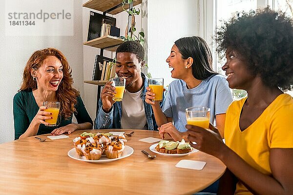 Multiethnische Freunde haben Spaß bei einem Frühstück mit Orangensaft und Muffins zu Hause